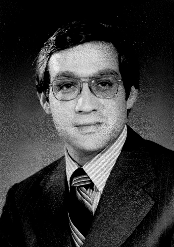 A black and white photo of Michael wearing 70s style glasses, a striped shirt, tie, and jacket